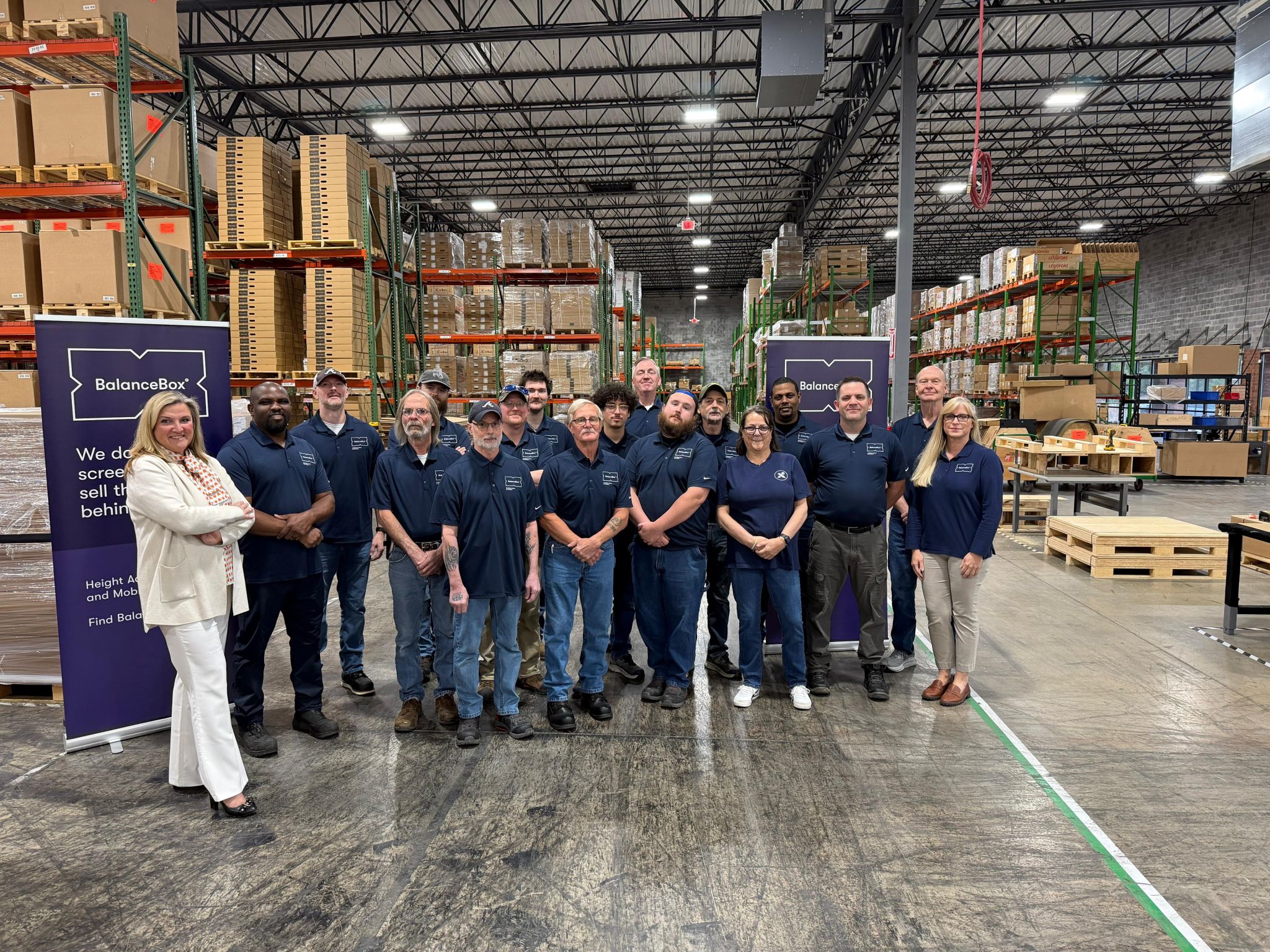 Group of people posing for a photo in a warehouse with BalancesBox branding.